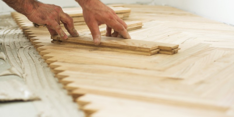 Handwerker verlegt Fischgrätparkett mit Holzleisten auf frischem Kleber.